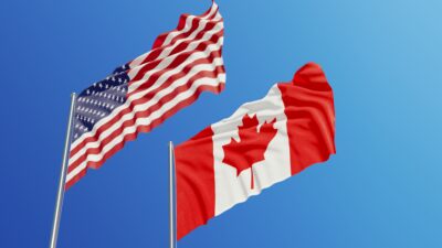 An image of the Canadian and American flags flying against a blue background.